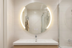 Modern bathroom with a round illuminated mirror above a sink.