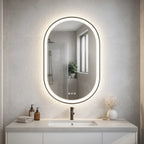 Bathroom vanity with a lit oval mirror reflecting a window and shower.